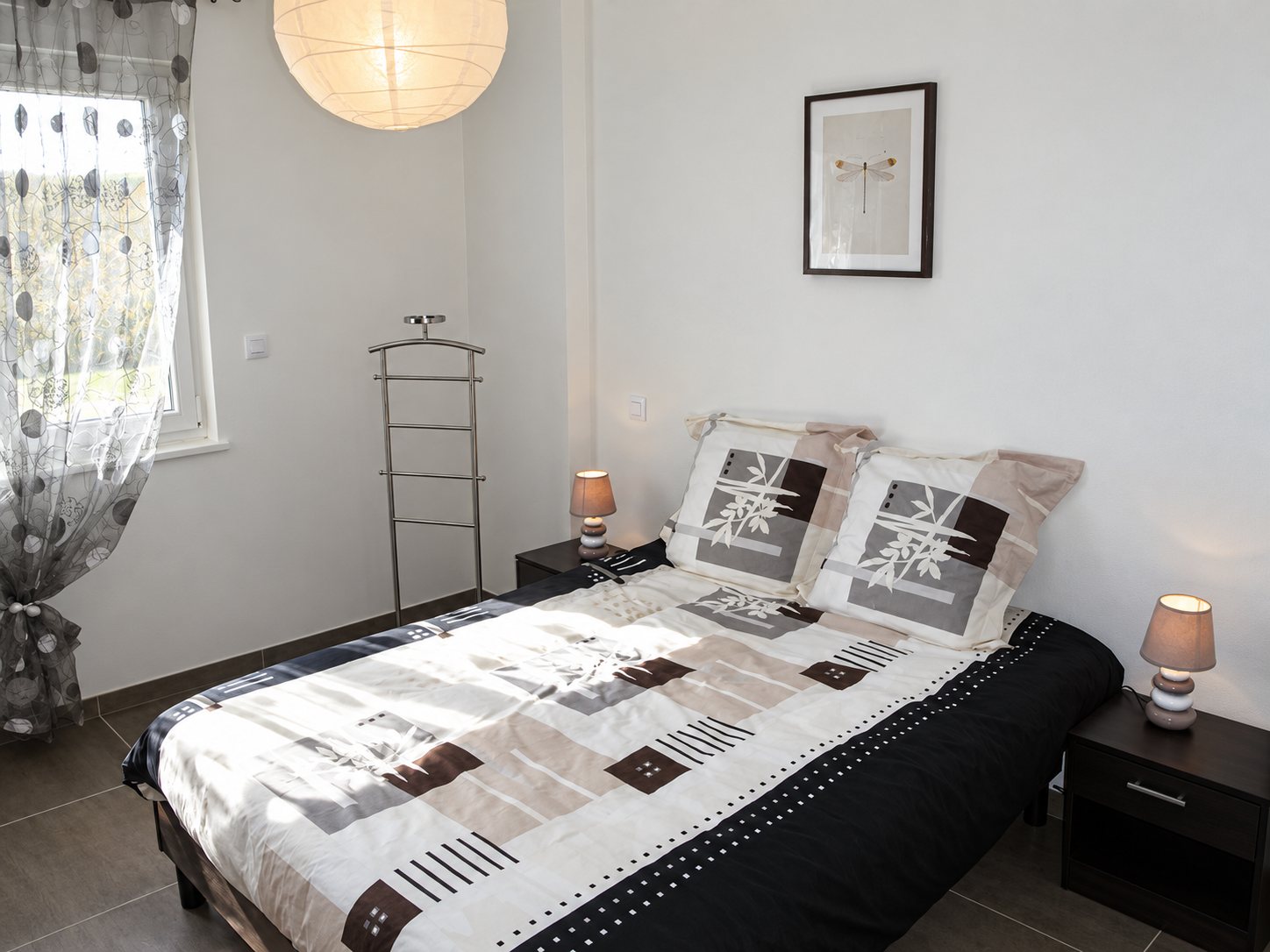 Chambre avec un lit double, rideau voilage et deux tables de chevet
